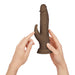 Hands holding a brown wireless Turbo Rabbit vibrator with dual stimulating heads and realistic texture.