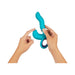 Hands holding a blue ergonomic triple action vibrator with curved tip and ring handle on white background.