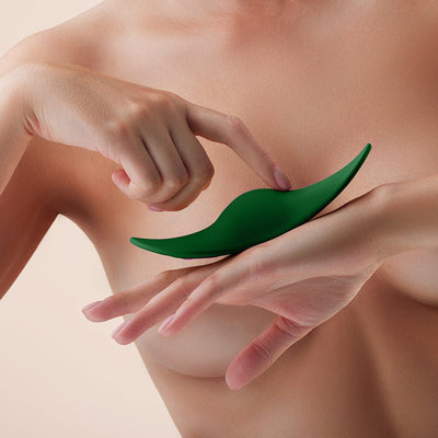 Close-up of a person holding and pressing a sleek, green, curved FemmeFunn Unda panty vibrator against their hand.