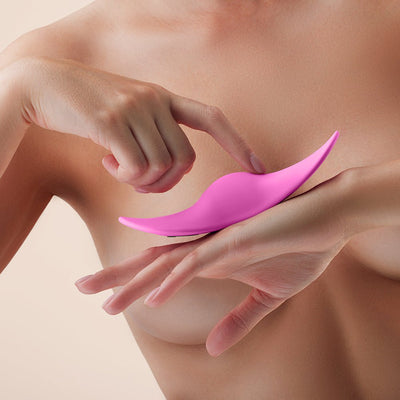 Close-up of a person holding and touching a sleek pink FemmeFunn Unda Panty Vibrator against a neutral background.