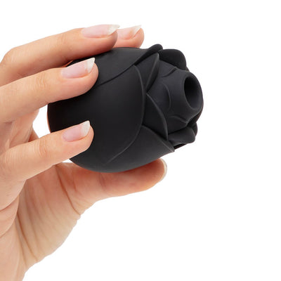 Hand holding a black rose-shaped clitoral suction stimulator with soft silicone petals and a central suction opening.