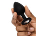 Hand holding a black silicone butt plug with a clear crystal base detail on a white background.
