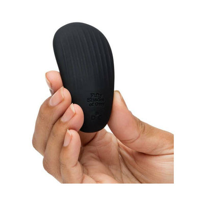 Hand holding a sleek black pebble-shaped Fifty Shades of Grey clitoral vibrator with textured surface.