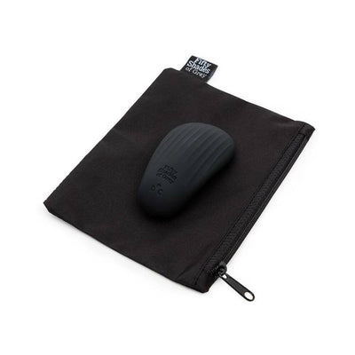 Pebble-shaped black silicone clitoral vibrator resting on a black zippered storage pouch with Fifty Shades of Grey tag.