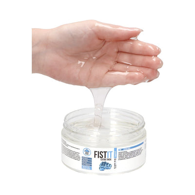 Hand holding thick clear water-based lubricant gel above an open jar of Fist It Extra Thick lube.