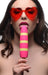 Woman wearing red heart-shaped sunglasses holding a pink and yellow striped silicone vibrator shaped like a popsicle.