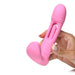 Hand holding a pink silicone G-spot vibrator with a flicking arm and smooth rounded tip against a white background.