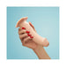Hand holding a vanilla-colored silicone dildo with a pronounced head and suction base against a light blue background.