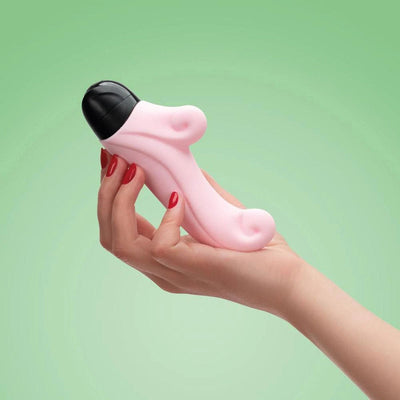 Hand holding a pink Fun Factory Ocean Rabbit mini vibrator with a black tip against a green background.