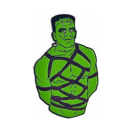 Green Frankenstein character enamel pin wearing black bondage harness straps.