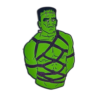Green Frankenstein character enamel pin featuring black bondage rope details and a somber expression.