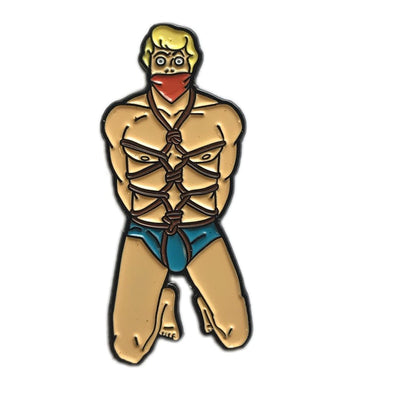 Enamel pin of a blonde man kneeling with ropes tied around his torso and a red gag over his mouth.