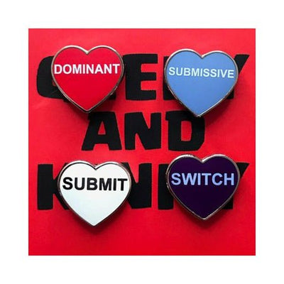 Set of four heart-shaped enamel pins labeled Dominant, Submissive, Submit, and Switch on a red background.