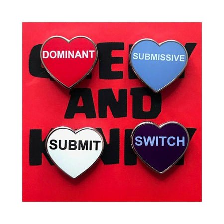 Set of four heart-shaped enamel pins labeled Dominant, Submissive, Submit, and Switch on a red background.