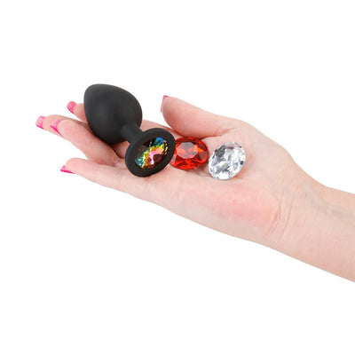 Hand holding a black silicone plug with a colorful gem and two additional interchangeable red and clear gems.