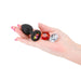 Hand holding a black silicone plug with three interchangeable colorful gem attachments in pink, red, and clear.