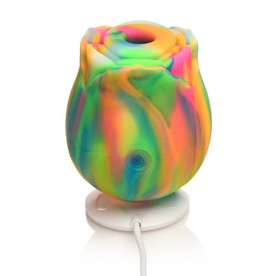 Rainbow-colored glow-in-the-dark rose clit stimulator on a white charging base with USB cable.