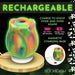 Rainbow-colored glow-in-the-dark rose clit stimulator on a magnetic charging base with USB cable.