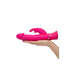 Hand holding a bright pink dual-density silicone rabbit vibrator with curved shaft and clitoral stimulator.