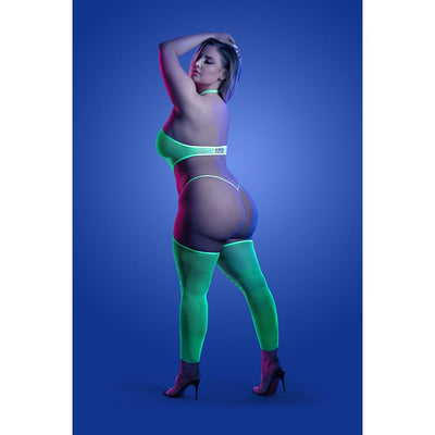 Curvy model wearing neon green UV reactive high neck bodystocking with matching G-string and thigh-high fishnet stockings against blue background.