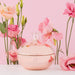 Highonlove Cannabis Body Butter in a round, rose gold jar surrounded by soft pink and peach flowers on a pink background.