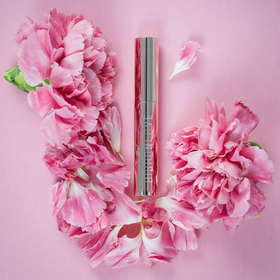 Highonlove Mini Lip Gloss tube surrounded by soft pink flower petals on a pastel pink background