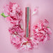 Highonlove Mini Lip Gloss tube surrounded by soft pink flower petals on a pastel pink background