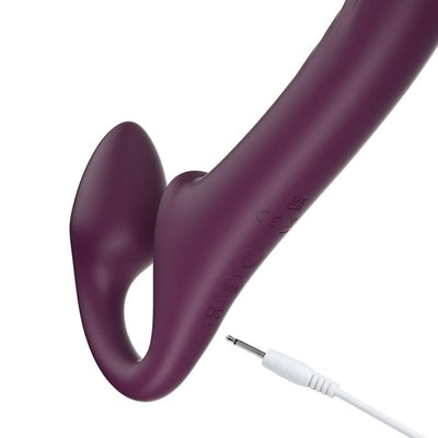 Deep purple strapless strap-on with curved rotating head and bulbous wearable shaft, shown with white USB charging cable.