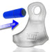 Clear silicone cock and ball sling with embossed logo and detachable blue bullet vibrator shown separately with directional arrow.