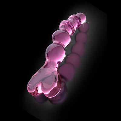 Pink hand-crafted glass massager with beaded shaft and heart-shaped handle on a black reflective surface.