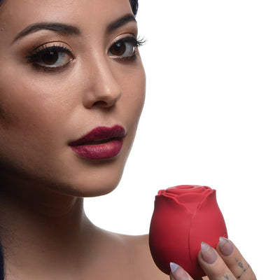 Close-up of a woman with bold makeup holding a red rose-shaped stimulator in her hand against a white background.