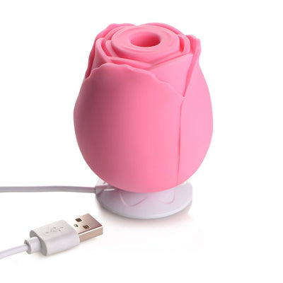 Pink rose-shaped silicone clitoral suction toy with USB charging cable on white background.