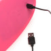 Close-up of pink silicone Inmi Spin N Grind toy being charged with a black USB cable on a white background.