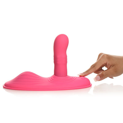 Pink silicone grinding pad with rotating shaft and textured mound, shown with a hand pressing the power button.