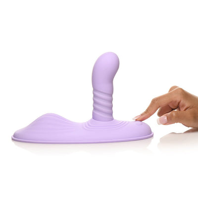 Hand pressing button on a curved, ribbed purple silicone adult toy with a wide base.