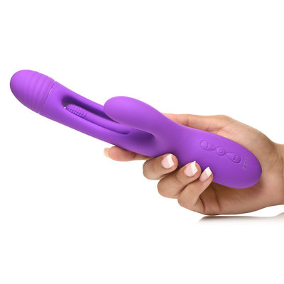 Hand holding a purple silicone Inmi Tri Flick rabbit vibrator with curved shaft, flicking arm, and control buttons.
