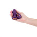 Hand holding a purple Inya Alpine remote-controlled butt plug with matching wireless remote on white background.