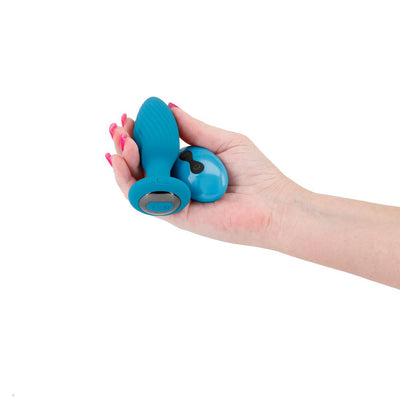 Hand holding a teal remote-controlled Inya Alpine butt plug with a textured surface and matching remote.