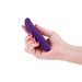 Hand holding a compact, dark purple bendable personal massager with a smooth silicone surface and subtle wave design.