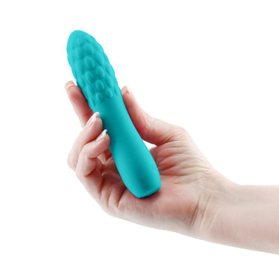 Hand holding a compact turquoise textured silicone vibrator with a rounded tip and pebble-like surface details.