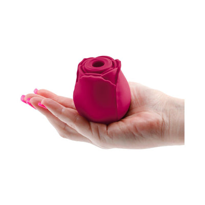 Hand holding a compact, deep pink rose-shaped silicone device with a central air stimulation opening.