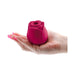 Hand holding a compact, deep pink rose-shaped silicone device with a central air stimulation opening.