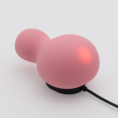 Pink snowman-shaped Iroha Yuki Nadeshiko Color vibrator on a black USB charging base with glowing light indicator.