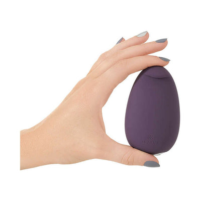Hand holding a compact, pebble-shaped purple Je Joue Mimi Soft clitoral vibrator with a smooth silicone surface.
