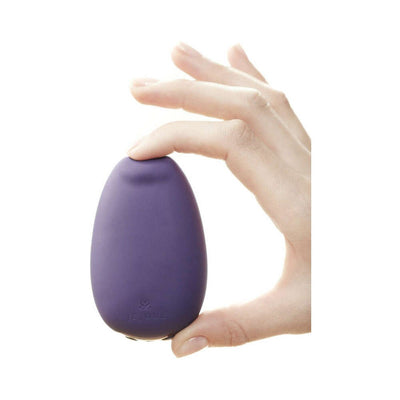 Hand holding the purple Je Joue Mimi Soft clitoral vibrator with a soft silicone tip against a white background.