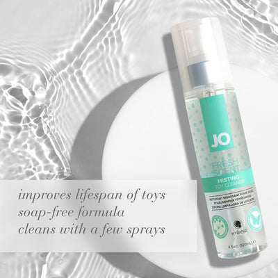 Bottle of JO Fresh Scent Misting Toy Cleaner with text highlighting soap-free formula and toy lifespan benefits on water ripple background.