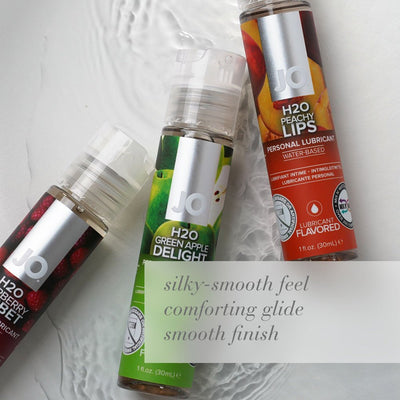 Three bottles of JO H2O flavored personal lubricants in green apple, peach, and raspberry flavors on a textured surface.