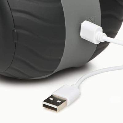 Close-up of a black and gray vibrating double masturbator with a USB charging cable plugged in.