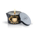 Kama Sutra Ignite Massage Candle 6oz in black tin with gold label, lit wick, and matching lid beside it.