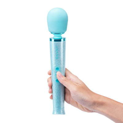Hand holding a glittery blue Le Wand Petite massager with rounded head and two-button control on white background.